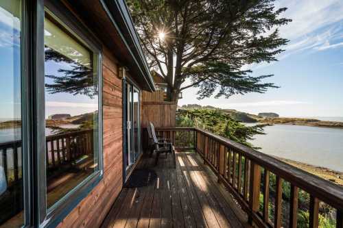 A wooden deck with a chair overlooks a serene coastal landscape and calm waters under a clear blue sky.