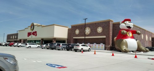 A large Buc-ee's store with a giant beaver mascot outside, surrounded by parked cars and a clear blue sky.