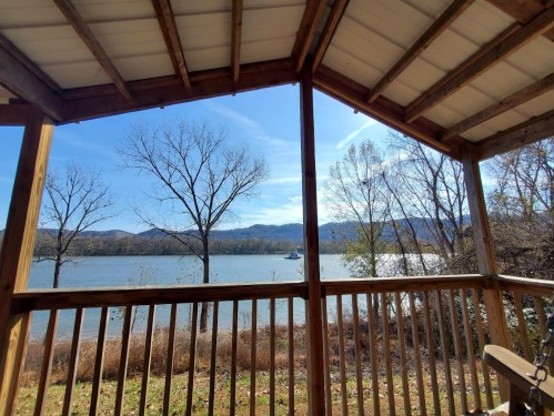 View of a serene lake framed by wooden beams, with trees and mountains in the background under a clear blue sky.