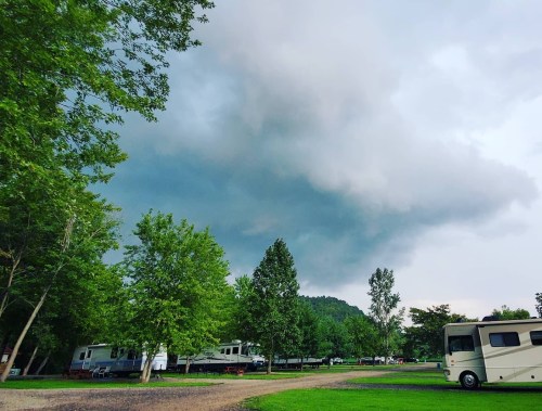 Dark clouds loom over a campground with RVs and trees, suggesting an approaching storm.