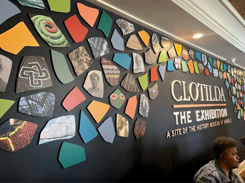 Colorful wall display featuring various images and patterns, with the text "CLOTTILDA THE EXHIBITION" prominently featured.