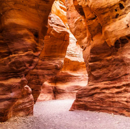 A narrow canyon with vibrant orange and red rock formations, creating a winding path through the landscape.