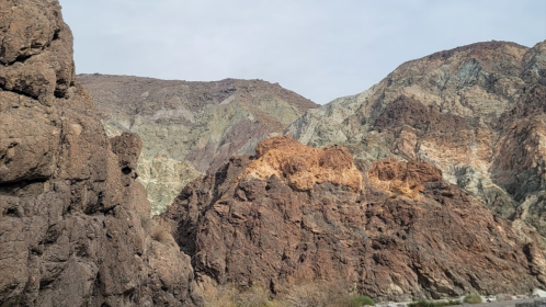 Rocky landscape with layered mountains in various earthy tones under a cloudy sky.