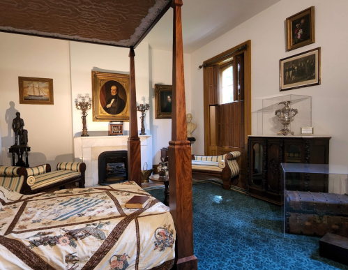 A vintage bedroom featuring a four-poster bed, ornate furniture, paintings, and decorative items in a cozy setting.
