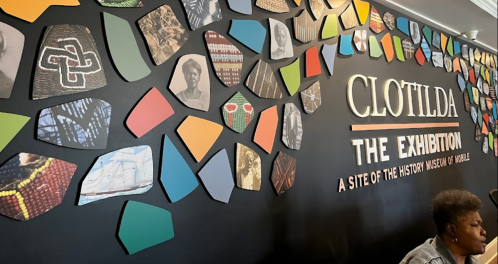 Colorful wall display featuring various images and patterns related to the Clotilda exhibition and African history.