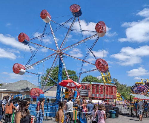 A colorful Ferris wheel at a fair, with people enjoying the rides under a bright blue sky.