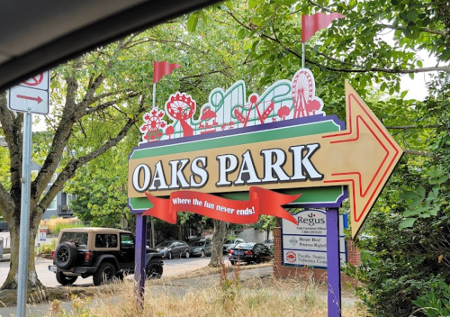 Colorful sign for Oaks Park with a fun slogan, featuring amusement park graphics and an arrow pointing right.
