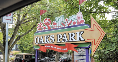 Colorful sign for Oaks Park with a fun design, featuring rides and attractions, and an arrow pointing to the entrance.