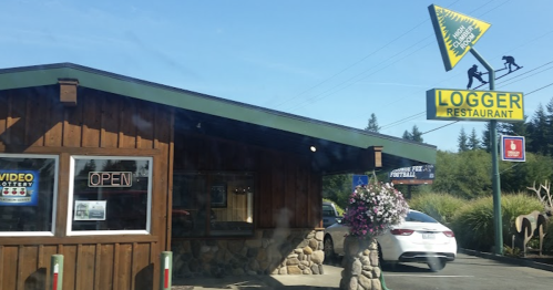 Exterior of Logger Restaurant with a wooden facade, open sign, and a large yellow sign featuring a logger.