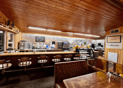 Cozy diner interior with wooden decor, a counter, and a display case filled with food. Warm, inviting atmosphere.