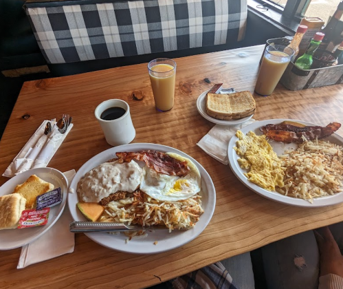 A table set with two plates of breakfast, coffee, orange juice, and toast, featuring eggs, bacon, hash browns, and biscuits.