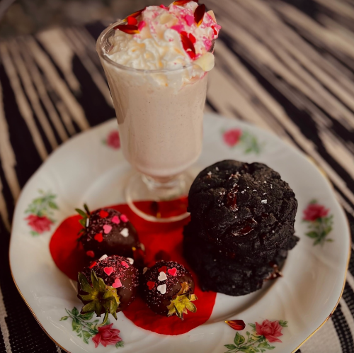A dessert plate featuring a milkshake, chocolate cookies, and strawberries topped with chocolate and sprinkles.