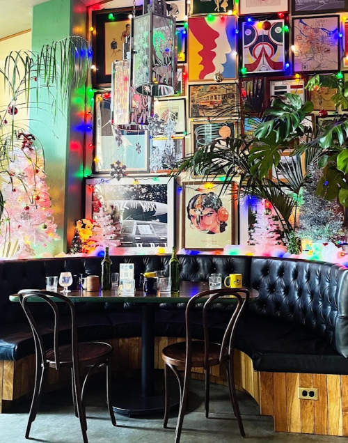 Cozy restaurant corner with a black leather booth, colorful artwork, and festive lights adorning the walls.
