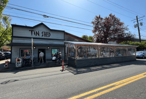 A restaurant named "Tin Shed" with outdoor seating, surrounded by trees and a clear blue sky.