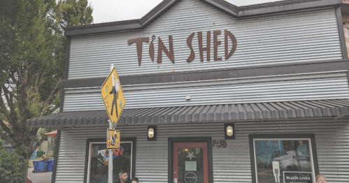 A gray building with "Tin Shed" sign, featuring a couple sitting outside and a "Black Lives Matter" sign in the window.