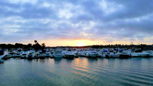 A serene marina at sunset, with boats docked and a colorful sky reflecting on the water.