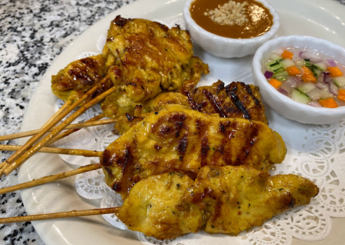 Grilled chicken skewers served with peanut sauce and a side of mixed vegetable salad on a white plate.