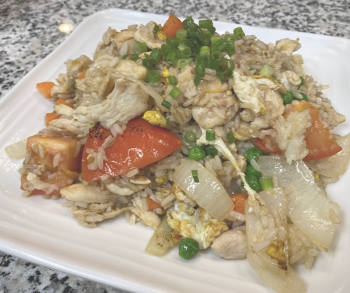 A plate of fried rice with chicken, tomatoes, onions, peas, and green onions, served on a white dish.