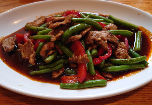 A plate of stir-fried beef with green beans and red bell peppers in a savory sauce.