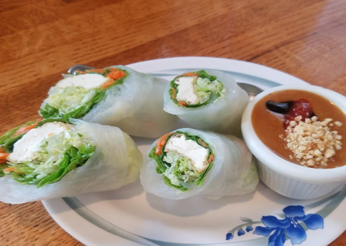 Fresh spring rolls filled with lettuce, carrots, and tofu, served with a side of peanut dipping sauce.