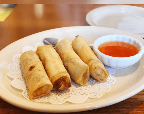 Three crispy spring rolls on a plate with a small bowl of dipping sauce.