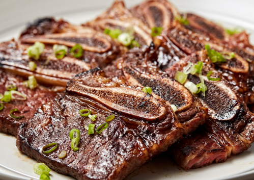 Grilled beef ribs garnished with chopped green onions on a white plate.