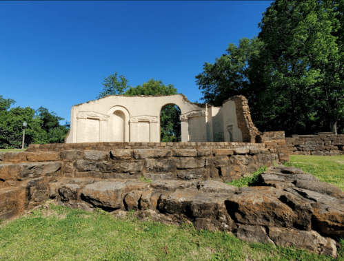 Ruins of a stone structure surrounded by greenery under a clear blue sky.