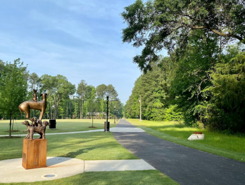 A pathway through a park lined with sculptures and greenery under a clear blue sky.