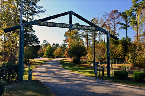 Entrance to Sherling Lake Park and Campground, surrounded by trees and a clear blue sky.