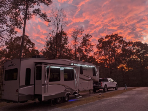 A camper parked under a vibrant sunset with trees in the background, creating a serene outdoor scene.