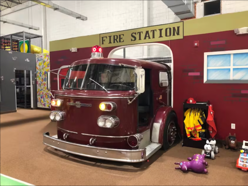A vintage red fire truck toy inside a play area, with colorful walls and various toys around it.