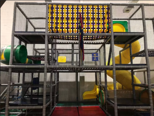 Colorful indoor play structure with slides, tunnels, and climbing areas, enclosed in safety netting.