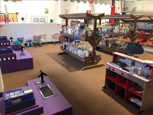 A colorful children's play market with shelves of toy groceries, cash registers, and a play kitchen setup.