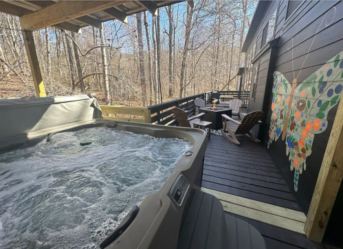 A hot tub on a deck surrounded by trees, with a colorful butterfly mural on the wall and outdoor seating nearby.