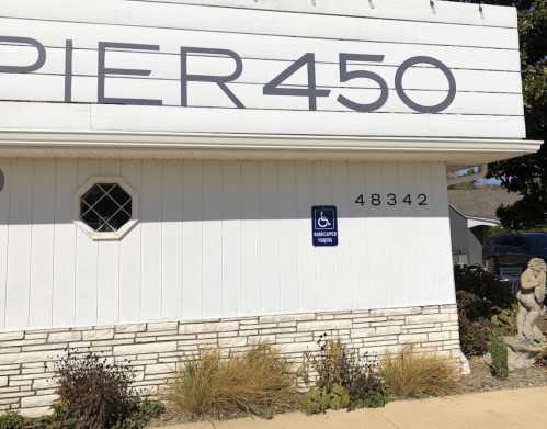 Sign for Pier 450 with a handicap parking symbol and the address 48342, next to decorative landscaping.