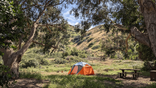 A colorful tent set up in a grassy area surrounded by trees and hills under a clear blue sky.