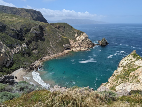 A scenic coastal view featuring cliffs, a sandy beach, and turquoise waters under a clear blue sky.