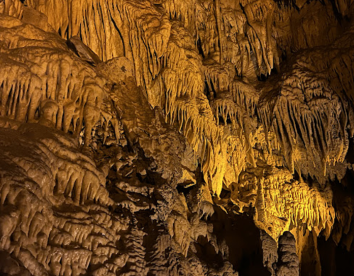 Stalactites and stalagmites in a dimly lit cave, showcasing intricate rock formations and warm lighting.