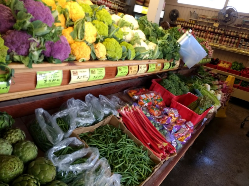 A vibrant display of fresh vegetables, including cauliflower, green beans, and herbs, in a market setting.
