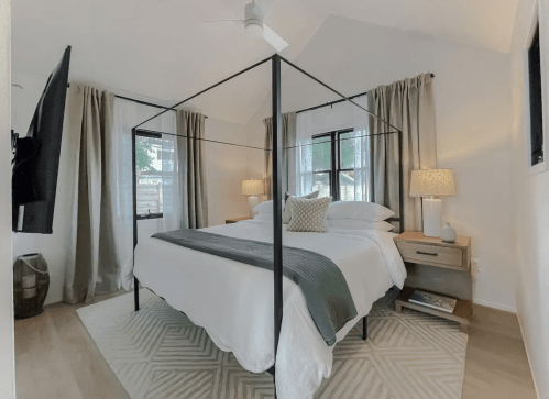 A modern bedroom featuring a four-poster bed, soft lighting, and large windows with curtains.