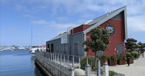 A waterfront building with a sign reading "Eppig Brewing," surrounded by boats and greenery along the shore.