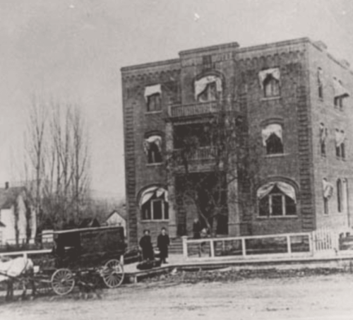 Historic building with large windows, two people standing outside, and a horse-drawn carriage in front.