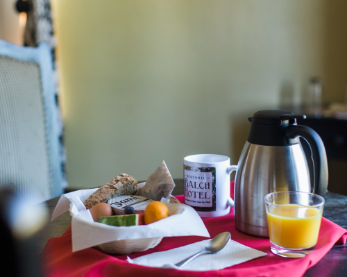 A breakfast spread with a coffee mug, a silver coffee pot, fruit, and a glass of orange juice on a table.