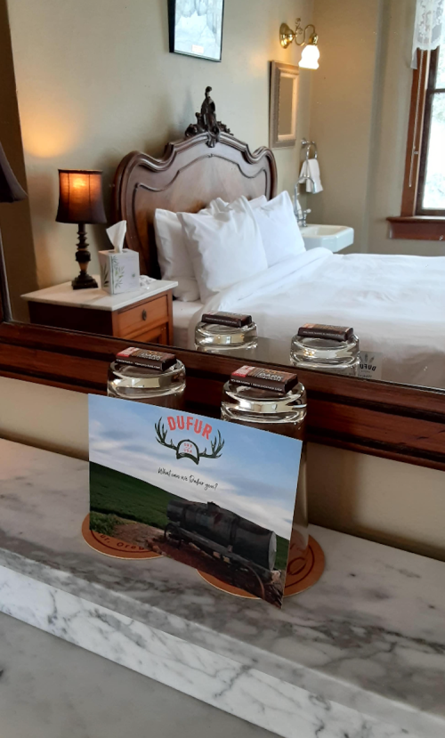 A cozy bedroom with a bed, lamp, and a mirror reflecting a postcard about Dufur, Oregon, on a marble surface.