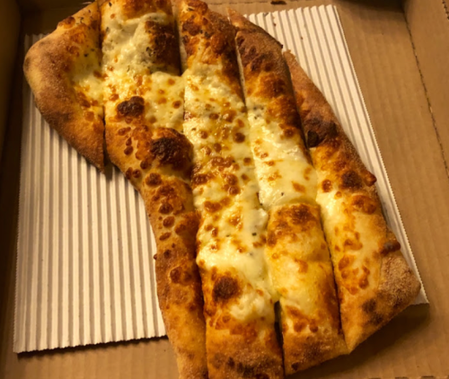 A slice of cheesy breadsticks with a golden crust, placed in a pizza box with a striped paper liner.