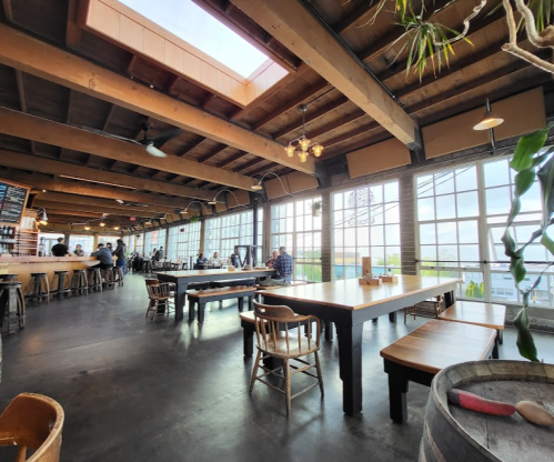 A spacious restaurant interior with large windows, wooden tables, and a cozy atmosphere.