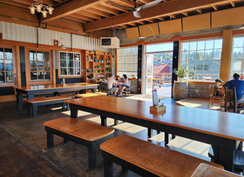 Bright, spacious interior of a restaurant with wooden tables, large windows, and patrons enjoying their meals.