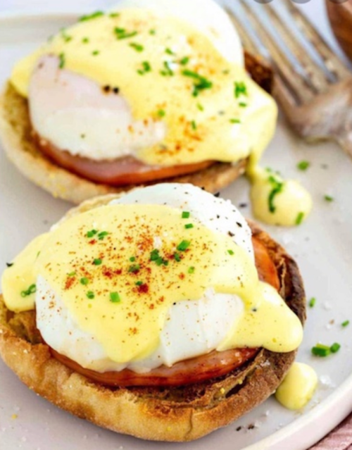 Two eggs Benedict on English muffins, topped with hollandaise sauce and sprinkled with chives and paprika.