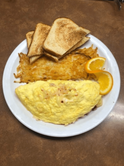 A plate with a fluffy omelette, golden hash browns, toasted bread, and orange slices.