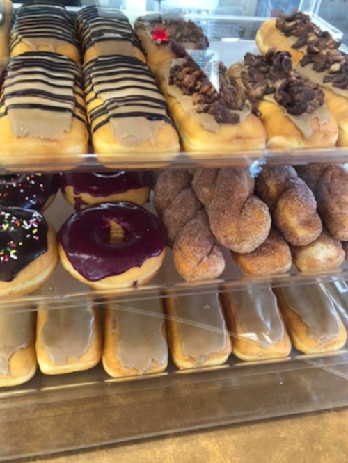 A display of assorted donuts, including chocolate-covered, glazed, and sprinkled varieties, stacked in a case.